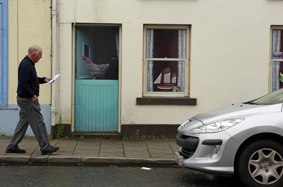 A man walks past an empty building, which has been covered with artwork to make it look more appealing, in the village of Bushmills on the Causeway Coast August 19, 2013. One of the homes of Irish whiskey has taken a scheme developed in Northern Ireland of erecting fake shop fronts where derelict buildings lie and has truly run with it in a bid to woo tourists. Bushmills, best known as the village where the whiskey of the same name was distilled for the first time 400 years ago, is now also becoming recognisable for the artwork and graphics that brighten up shop fronts left empty during the economic downturn. Picture taken August 19, 2013. REUTERS/Cathal McNaughton (NORTHERN IRELAND - Tags: BUSINESS SOCIETY TRAVEL) ATTENTION EDITORS: PICTURE 12 OF 20 FOR PACKAGE 'NORTHERN IRELAND'S TROMPE L'OEIL' SEARCH 'BUSHMILLS ART' FOR ALL IMAGES