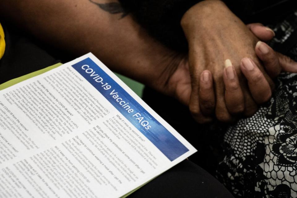 A vaccine information sheet is seen as Andrea Moore and Alma Penn, mother and daughter, hold hands while awaiting their COVID-19 vaccine in the gymnasium at Whitney M. Young Elementary School on April 2, 2021 in Louisville, Kentucky. (Photo by Jon Cherry/Getty Images)