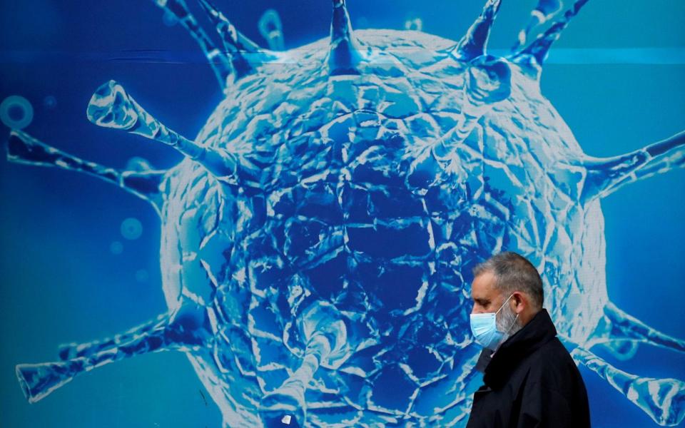 A man wearing a protective face mask walks past an illustration of a virus outside a regional science centre - Phil Noble /REUTERS