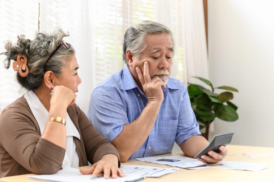 Two visibly concerned people using a calculator while examining bills and financial statements.