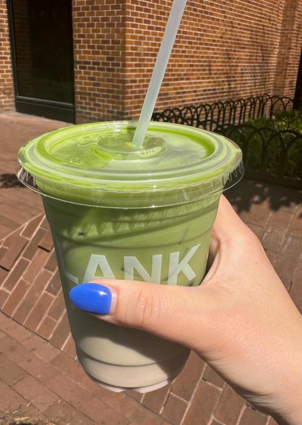Hand holding a plastic cup of green smoothie with a clear straw