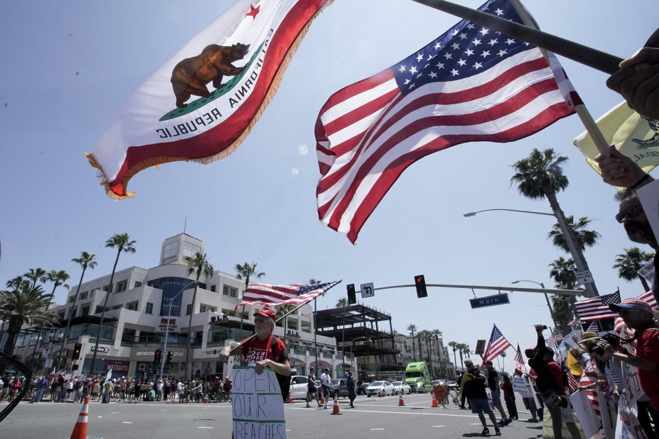 Protestors hold signs and wave flags during a May Day demonstration at the pier, Friday, May 1, 2020, in Huntington Beach, Calif. (AP Photo/Chris Carlson)