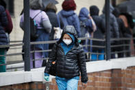 A medical worker wearing a single protective glove and a face mask walks past a line of workers and visitors waiting to be tested for COVID-19, the disease caused by the new coronavirus, at the main entrance to the Department of Veterans Affairs Medical Center, Monday, March 23, 2020, in New York. (AP Photo/John Minchillo)