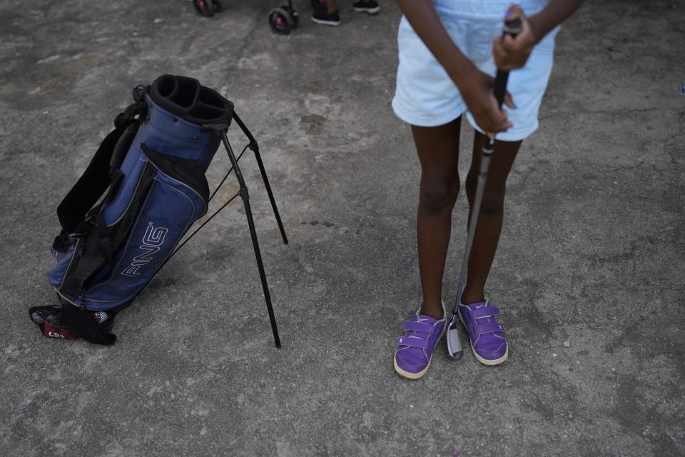 CORRECTS CADDIE'S SURNAME - A girl holds a golf putter on the grounds of the Nusacquilombo cultural center where children are learning the basics from caddie Marcelo Modesto, in Cidade de Deus or City of God favela, in Rio de Janeiro, Brazil, Thursday, Dec. 9, 2021. Modesto from one of Rio's poorest neighborhoods works at one of the seaside city's most exclusive golf courses, earning a comfortable living guiding wealthy patrons around the fairways and greens of the course. Now he is sharing his golf skills with kids from his favela. (AP Photo/Silvia Izquierdo)