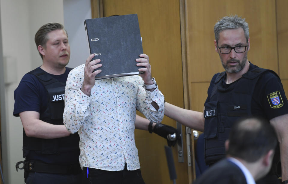 At the opening of the trial, the defendant covers his face with a folder as he arrives in the courtroom at the Higher Regional Court (OLG) in Frankfurt, Germany, Friday, April 24, 2020. The 37-year-old Iraqi defendant on suspicion of the murder of a five-year-old girl in Syria . The Federal Prosecutor's Office also charges him with genocide, membership of a terrorist organisation and human trafficking. (Arne Dedert/Pool via AP)