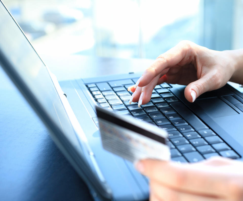 Closeup shot of unrecognisable woman entering credit card number to make a purchase online. She's using a blue coloured laptop. Credit card is in her left hand.