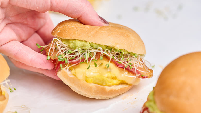 hand picking up breakfast slider with eggs, bacon, and avocado