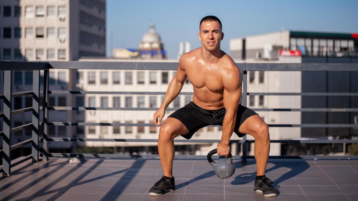  Man outside on balcony squatting with a kettlebell in left hand. 