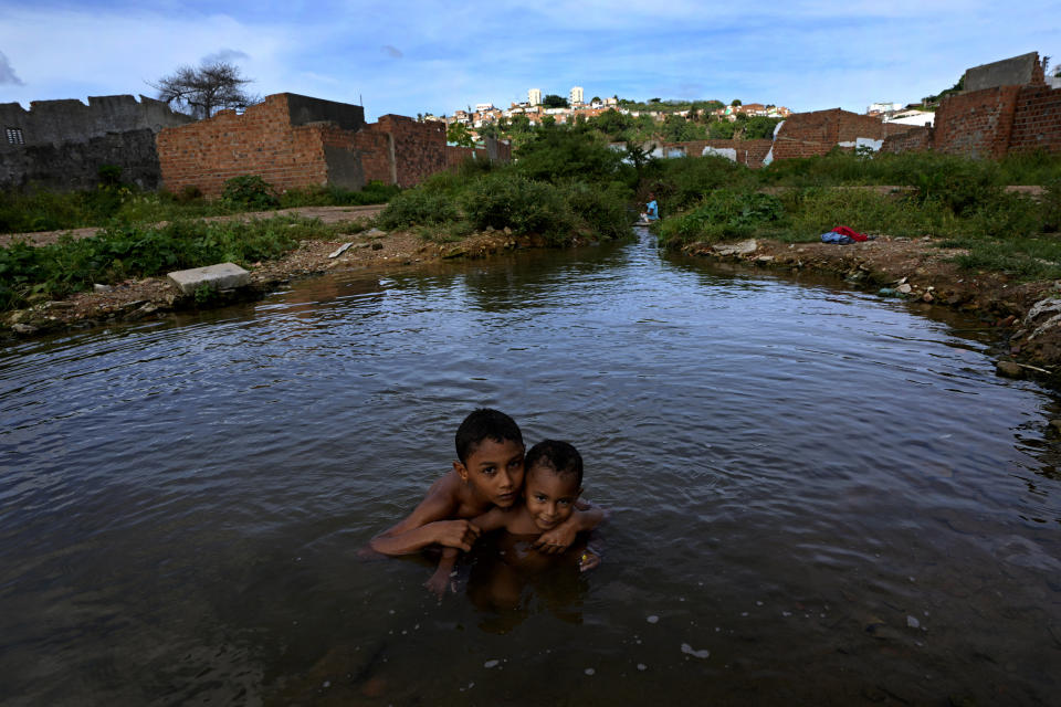 Children play in a pond at the Bom Parto neighborhood of Maceio, Alagoas state, Brazil, Monday, March 7, 2022. The homes in the neighborhood have been abandoned because they are threatened by ground subsidence caused by the Braskem mine that has forced more than 55 thousand people from their homes in Maceio. (AP Photo/Eraldo Peres)