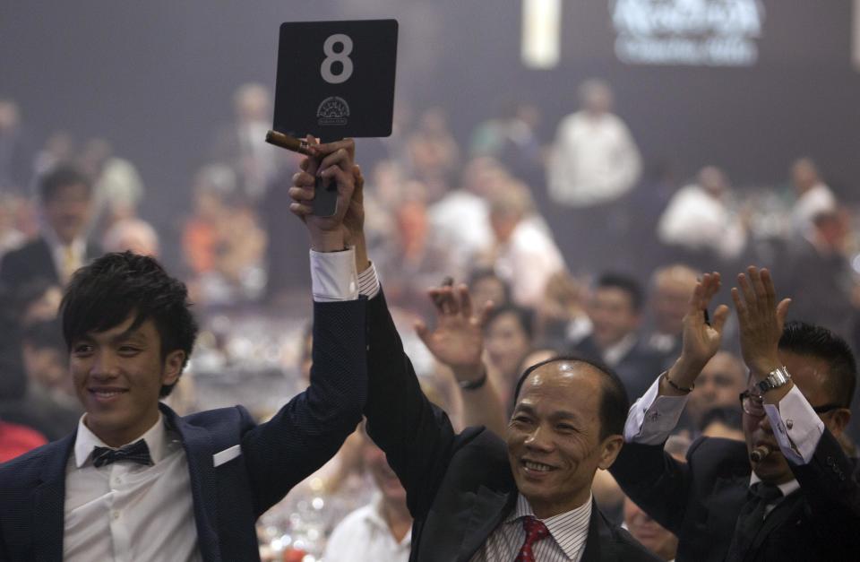 The exclusive distributor of Cuban Cigars in Macau Henry Leong Chi Hang, left, and an unidentified member of his group, participate in an auction of humidors during a gala dinner marking the end of the 16th annual Cigar Festival in Havana, Cuba, Friday, Feb. 28, 2014. Cigar aficionados have paid more than €798,000 ($1.1 million) for six handmade Cuban humidors at the gala closing of Havana's 16th annual Cigar Festival, a five-day bash that brings together hundreds of cigar sophisticates from around the world. The hot item was a one-of-a-kind handcrafted humidor packed with Montecristo cigars that fetched €170,000 ($235,000). (AP Photo/Franklin Reyes)