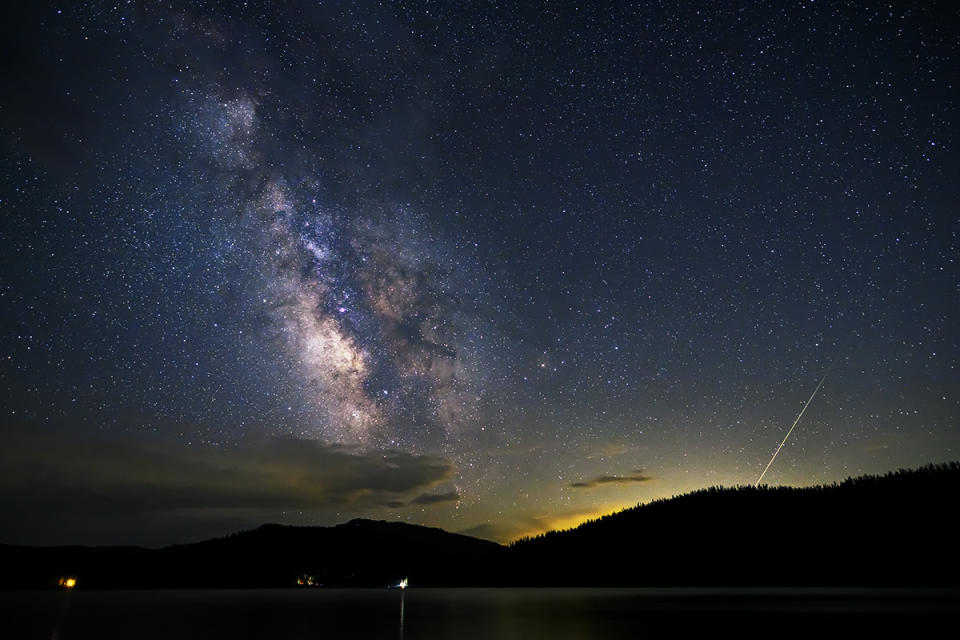 A meteor shower is pictured against a starry sky and picturesque foreground