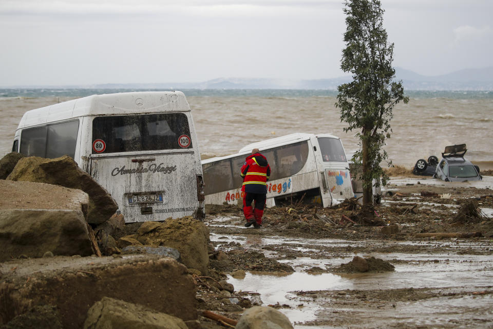 A rescuer walks next to vehicles carried away after heavy rainfall triggered landslides that collapsed buildings and left as many as 12 people missing, in Casamicciola, on the southern Italian island of Ischia, Saturday, Nov. 26, 2022. Firefighters are working on rescue efforts as reinforcements are being sent from nearby Naples, but are encountering difficulties in reaching the island either by motorboat or helicopter due to the weather. (AP Photo/Salvatore Laporta)