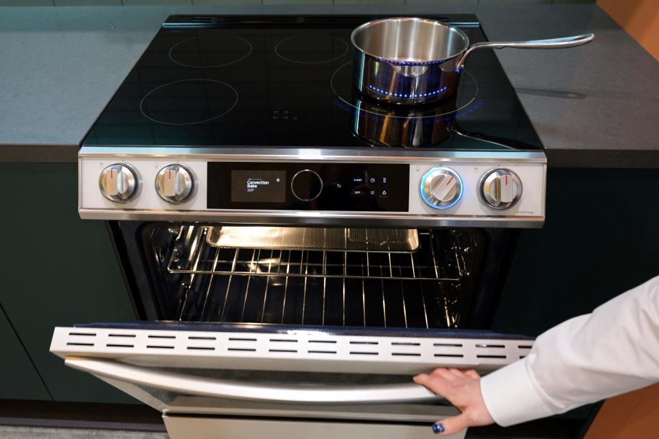 A pot sits on a burner as a product expert demonstrates an electric induction stove cooktop.