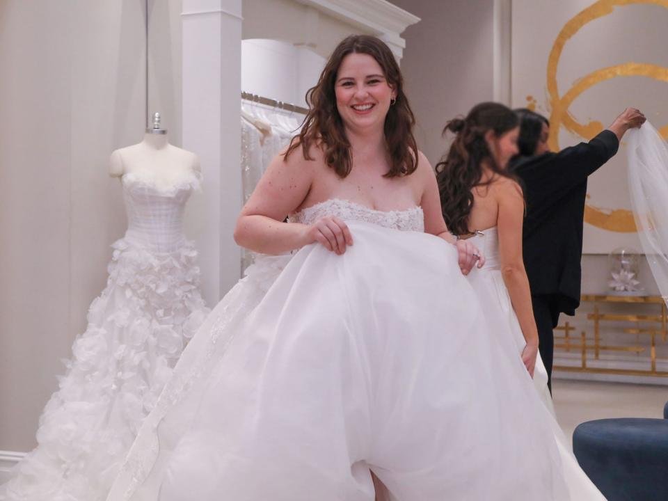 A woman walks through a bridal shop carrying a wedding dress.