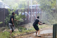 Squatters throw objects to prevent riot police from entering an abandoned school before being evicted, on the outskirts of Rome, Monday, July 15, 2019. Residents set fire early Monday to mattresses and other garbage to form a barrier and prevent riot police from entering the building but authorities doused the blaze and proceeded with the eviction. (Massimo Percossi/ANSA via AP)