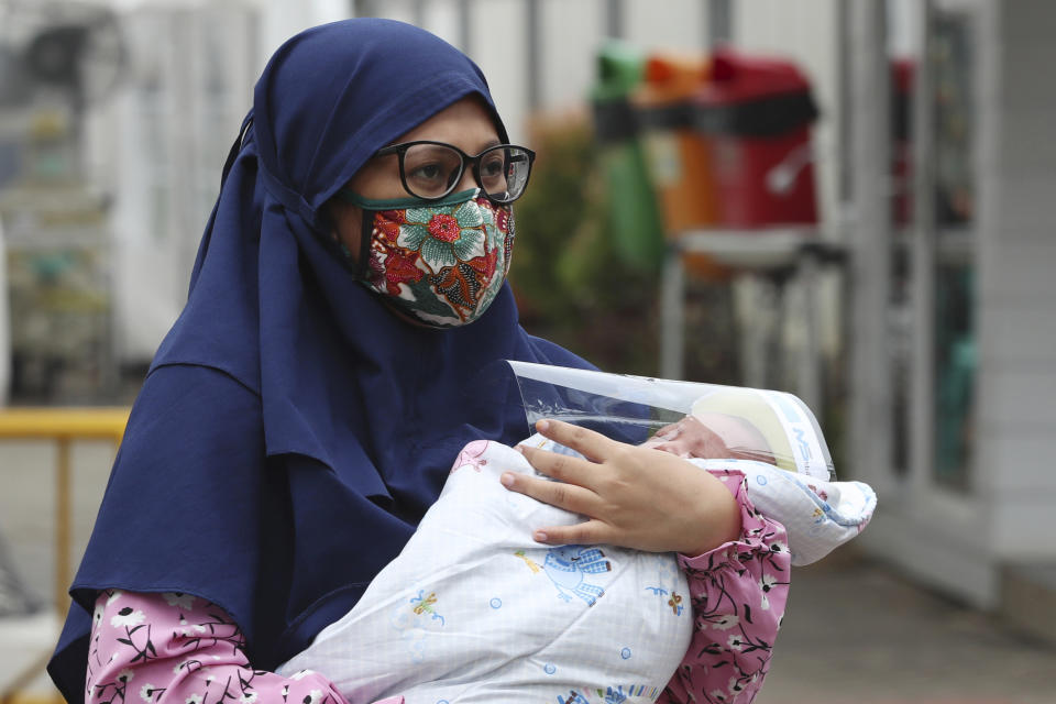 A Muslim woman carries her baby with face shield at a hospital in Jakarta, Indonesia, Tuesday, April 28, 2020. The world's Muslims have begun Ramadan with dawn-to-dusk fasting amid restrictions imposed to slow the pandemic that left many confined to their homes and public venues like parks, malls and even mosques are shuttered. (AP Photo/Achmad Ibrahim)