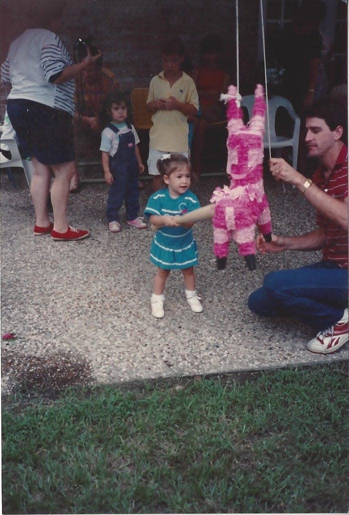 Dad holds a piñata as 2-year-old me takes a swing in 1989.