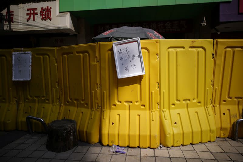 Signs advertising vegetables, rice and oil for sale on a barrier set up to ring fence a wet market on a street in Wuhan