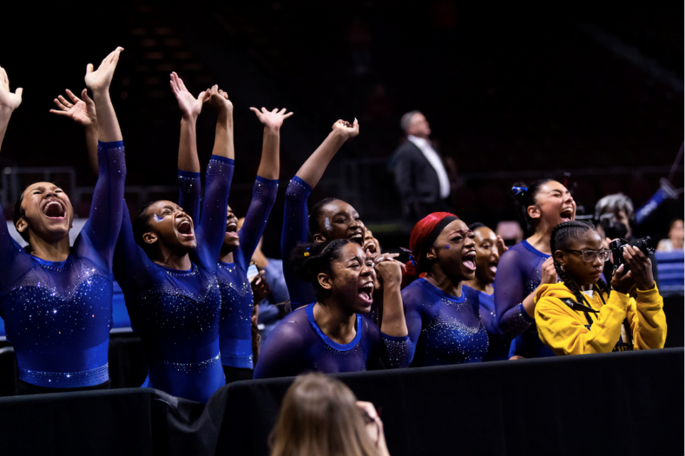 Members of Fisk University's gymnastics team cheering on the sidelines as one of their teammates competes.