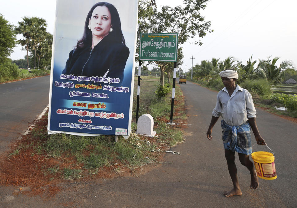 A villager carries a bucket of water and walks past a hoarding featuring U.S. democratic vice presidential candidate Sen. Kamala Harris at a crossing in Thulasendrapuram village, south of Chennai, Tamil Nadu state, India, Wednesday, Nov. 4, 2020. The villagers on Tuesday held special prayers for Harris' success in the elections at the temple in this lush green village, the hometown of Harris' maternal grandfather who migrated from here decades ago. The hoarding in Tamil reads, "From Thulasendrapuram to America, we wish the American vice presidential candidate hailing from Thulasendrapuram village Kamala Harris victory in the elections- From the villagers of Thulasendrapuram." (AP Photo/Aijaz Rahi)