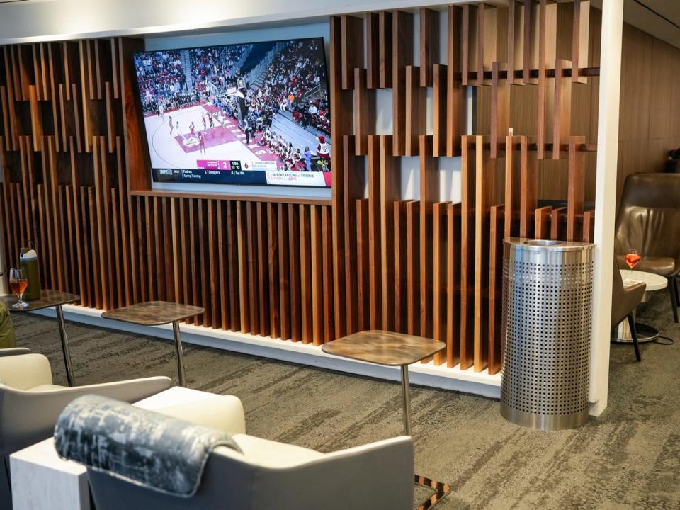 Gray lounge chairs with brown tables in front of them and a TV with a basketball game on the screen hanging in front of them