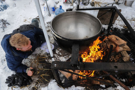 A man makes a fire under a large cooking pot in the Oceti Sakowin camp during a protest against plans to pass the Dakota Access pipeline near the Standing Rock Indian Reservation, near Cannon Ball, North Dakota, U.S. November 29, 2016. REUTERS/Stephanie Keith