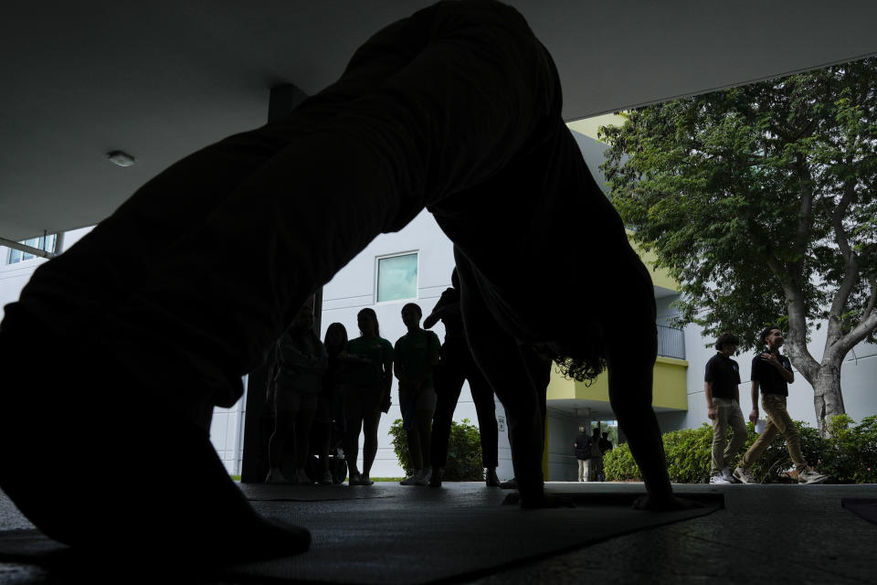 Miami Arts Studio students passing between classes look on as Gavin Perez practices yoga poses as part of an event to raise awareness about mental health, on World Mental Health Day, Tuesday, Oct. 10, 2023, at Miami Arts Studio, a public 6th-12th grade magnet school, in Miami. (AP Photo/Rebecca Blackwell)