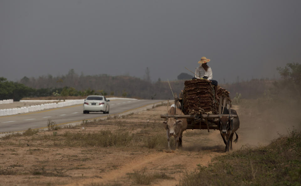 In this March 29, 2013 photo, a car travels in the highway that connects Yangon to capital Naypyidaw as a cart pulled by bulls carry a load in a parallel gravel track, close to Toungoo, north of Yangon, Myanmar. Vehicles are still out of the reach of all but a few in Myanmar, where annual incomes average $200. (AP Photo/Gemunu Amarasinghe)