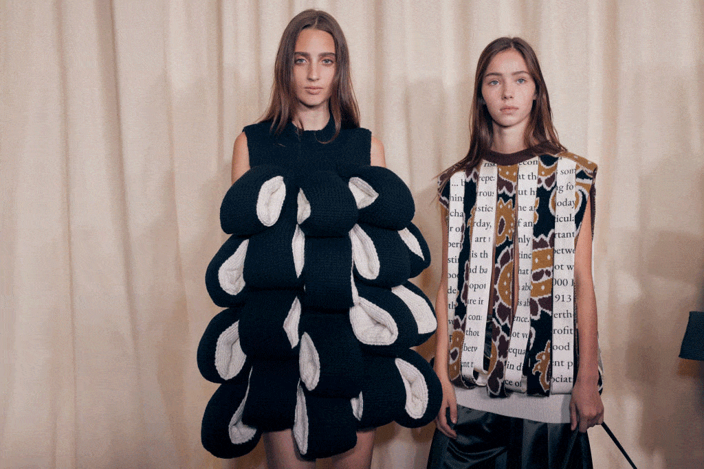 two models wearing sweater vests standing in front of a white curtain