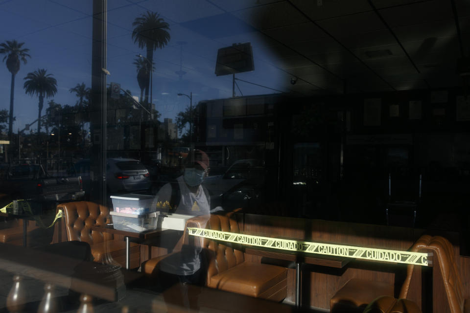 A man wearing a mask is reflected in the window of a restaurant with caution tape around its booths amid the coronavirus pandemic in the Westlake neighborhood of Los Angeles, Thursday, May 21, 2020. While most of California took another step forward to partly reopen in time for Memorial Day weekend, Los Angeles County didn't join the party because the number of coronavirus cases has grown at a pace that leaves it unable to meet even the new, relaxed state standards for allowing additional businesses and recreational activities. (AP Photo/Jae C. Hong)