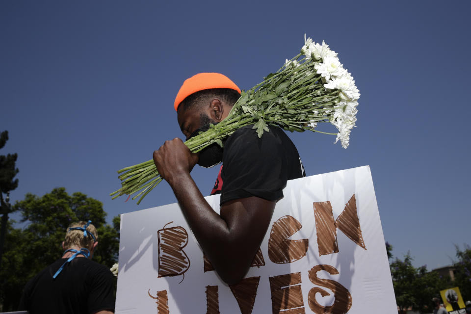 FILE - In this July 20, 2020, file photo, holding flowers and a sign, Blair Toles, 30, attends rally in Los Angeles, on Black Strike Day. Ahead of Labor Day, major U.S. labor unions say they are considering work stoppages in support of the Black Lives Matter movement. (AP Photo/Jae C. Hong, File)