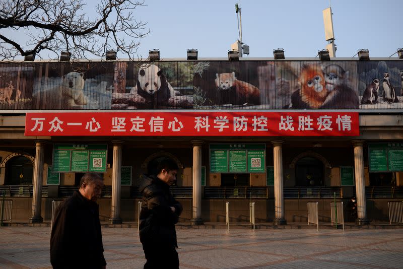 FILE PHOTO: Men walk past a banner hung on the ticket office of the Beijing Zoo that is closed following an outbreak of the novel coronavirus in the country, in Beijing