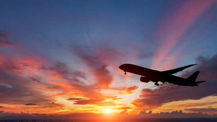 Airplane silhouette in the sky with clouds and a sun setting behind it