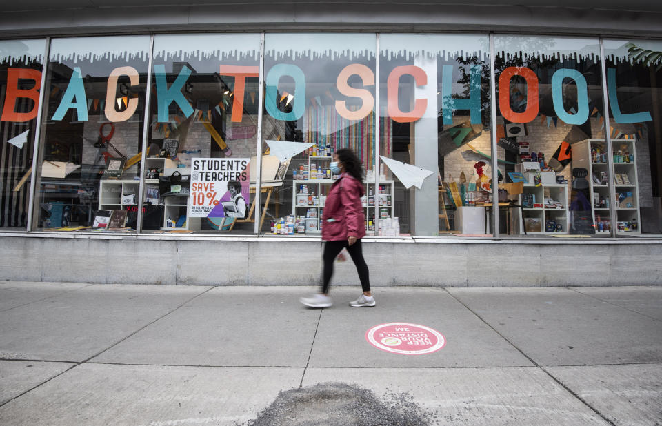 A person in a face mask walks past a storefront advertising their back to school sale, in Ottawa, Ontario, on the Labour Day long weekend, Monday, Sept. 7, 2020, in the midst of the COVID-19 pandemic. (Justin Tang/The Canadian Press via AP)