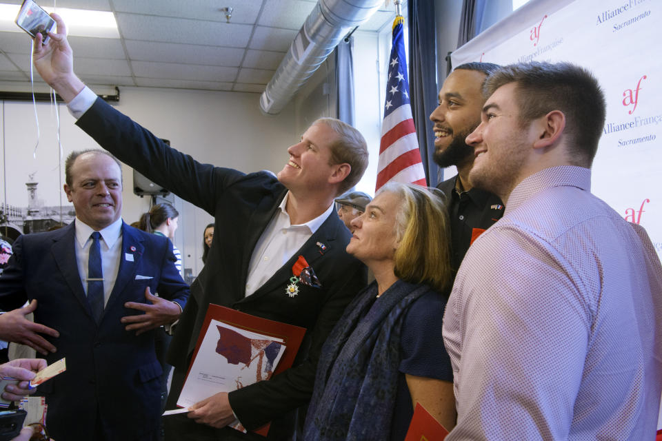 Spencer Stone, left holding the camera, photographs himself and French Conseillere Consulaire Sophie Lartilleux-Suberville, Anthony Sadler, and Alek Skarlatos following a French Naturalization Ceremony in Sacramento, Calif., Thursday, Jan. 31, 2019. The three men were heralded as heroes when they subdued an armed terrorist on a train in France in 2015. Today they were granted French citizenship. (AP Photo/Randall Benton)