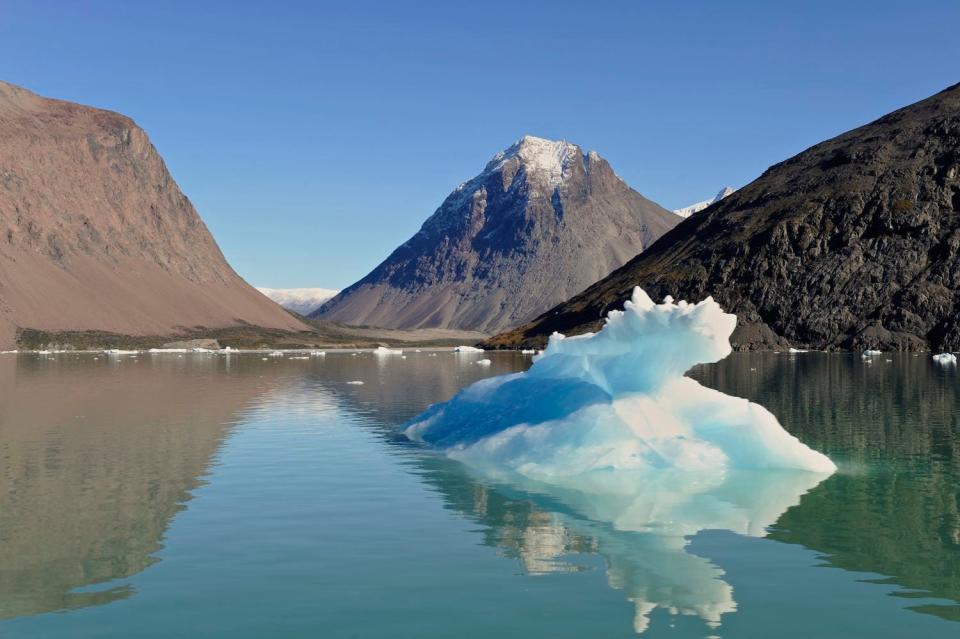 A picture shows a small iceberg floating on a pond. In the background are mountains in Southern Greenland.