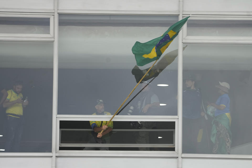 A protesters, supporter of Brazil's former President Jair Bolsonaro, waves a Brazilian national flag from a window after storming the Planalto Palace in Brasilia, Brazil, Sunday, Jan. 8, 2023. Planalto is the official workplace of the president of Brazil. (AP Photo/Eraldo Peres)