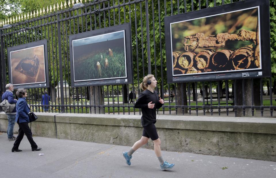 A woman runs next to " "A rusting rifle" a picture by British photographer Michael St Maur Sheil at the Paris Luxembourg gardens, Tuesday, April 8, 2014 as part of an exhibition " Fields of Battle - Lands of Peace 14-18 ". Captured over a period of seven years, Michael’s photography combines a passion for history and landscape and presents a unique reflection on the transformation of the battlefields of the Great War into the landscape of modern Europe. (AP Photo/Christophe Ena)