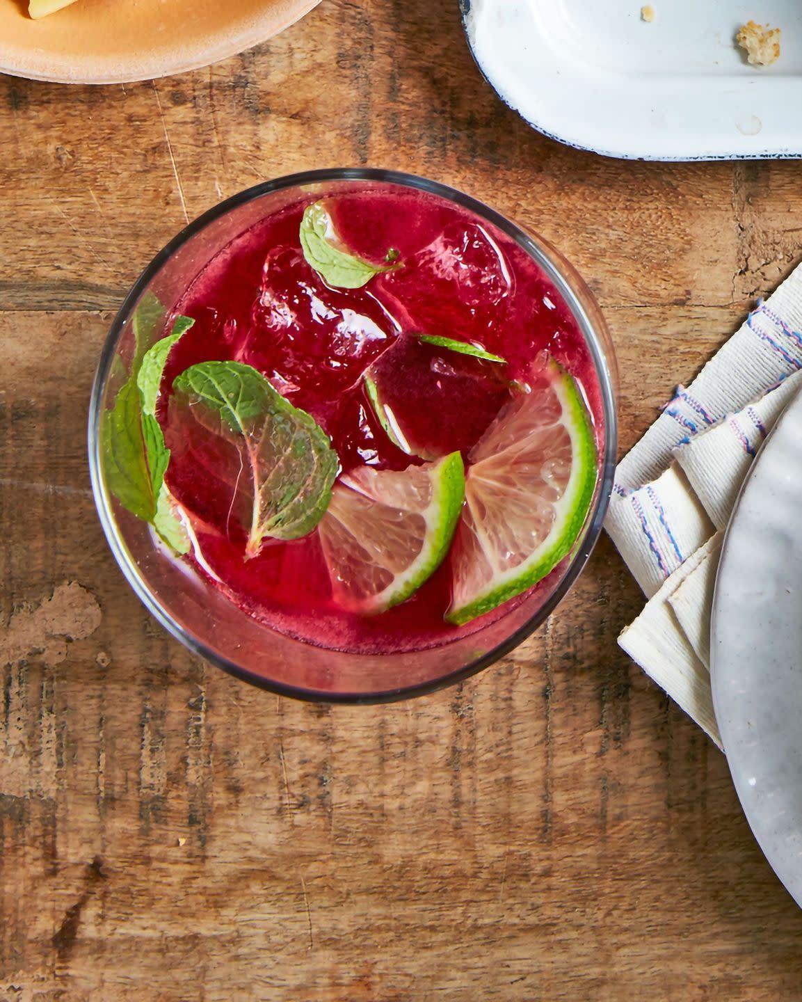 blackberry jam cocktail in a glass with ice lime slices and mint leaves