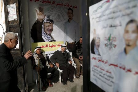 Palestinians sit next to posters praising a man who was killed after attempting to run over Israeli soldiers at the village of Beit Omar near the West Bank city of Hebron November 29, 2015. REUTERS/Baz Ratner