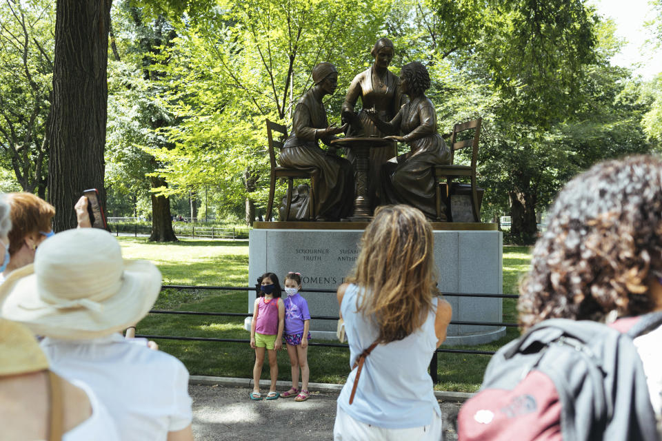 Visitors interact with the Women's Rights Pioneers statue in Central Park Wednesday, Aug. 26, 2020, in New York. The statue, created by sculptor Meredith Bergmann and featuring Sojourner Truth, Susan B. Anthony and Elizabeth Cady Stanton, is the first monument in the park honoring any female historical figures. (AP Photo/Kevin Hagen)