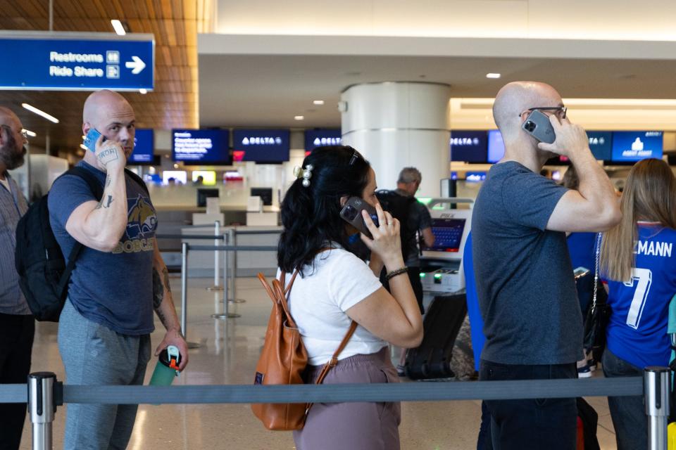 Travelers make phone calls while waiting in line for information on their delayed or canceled flights on July 19, 2024, at Sky Harbor Airport in Phoenix.