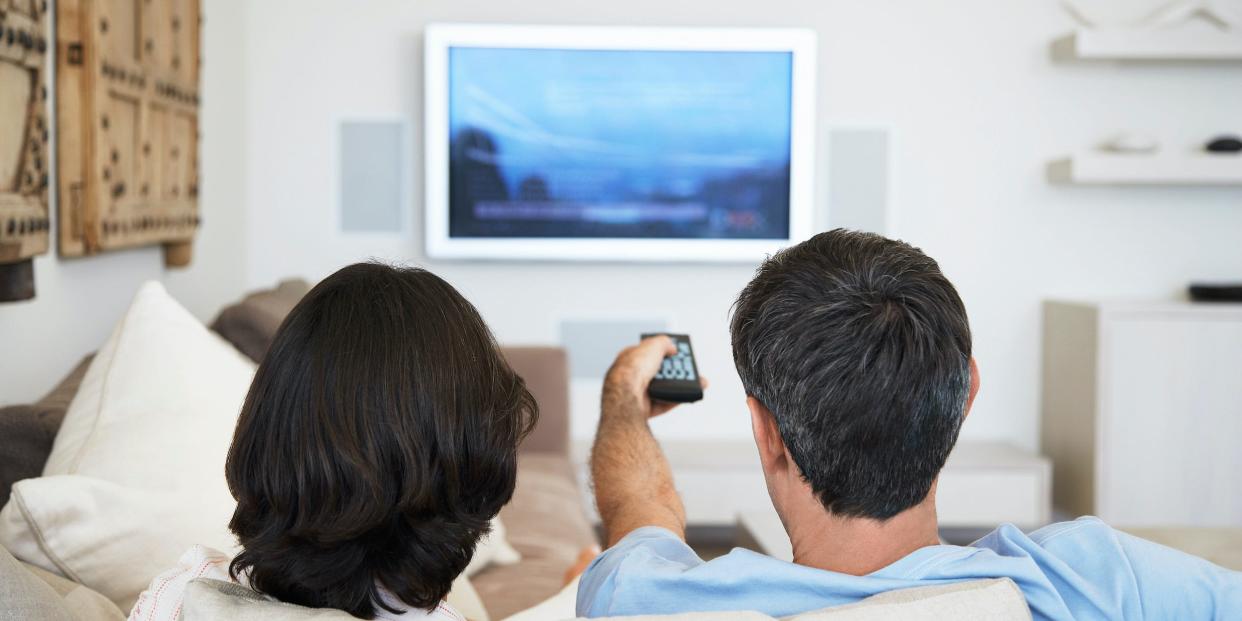 couple on couch watching TV at home with remote in hand