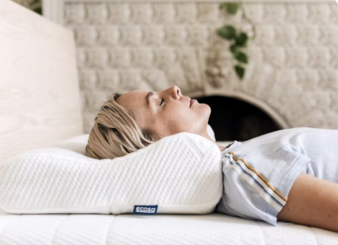 A man lies in side view on a contoured pillow with a white brick fireplace in the background.