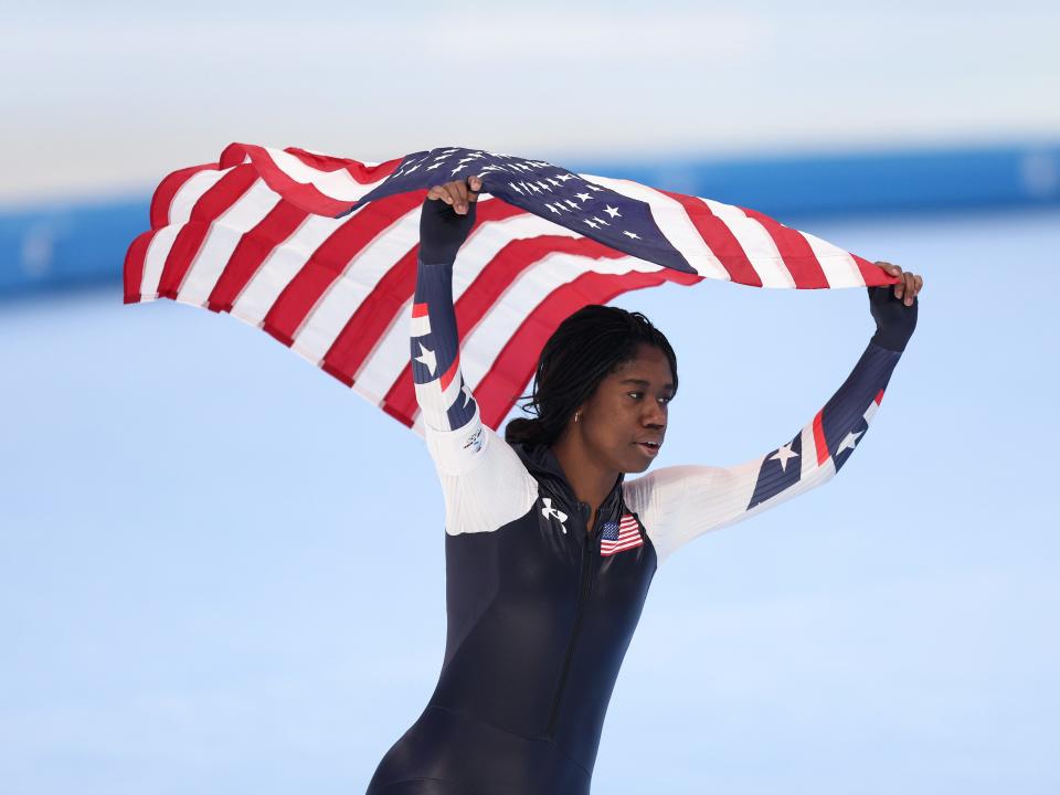 Speed skater Erin Jackson carrying American flag above her head after winning gold medal