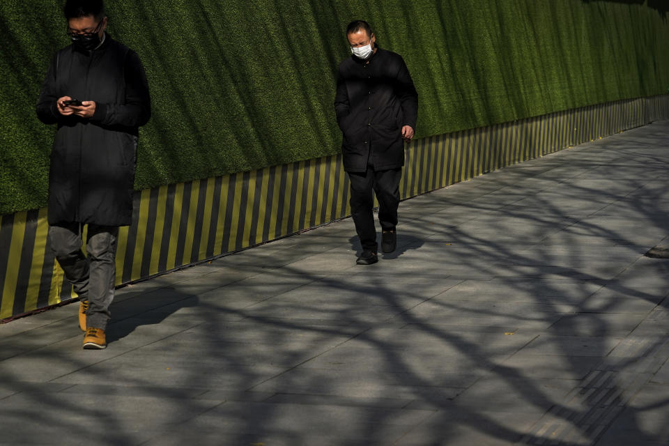 People wearing face masks to help curb the spread of the coronavirus walk by tree shadows at the Central Business District in Beijing, Tuesday, Nov. 24, 2020. China has reported new coronavirus cases in the cities of Shanghai and Tianjin as it seeks to prevent small outbreaks from becoming larger ones. (AP Photo/Andy Wong)
