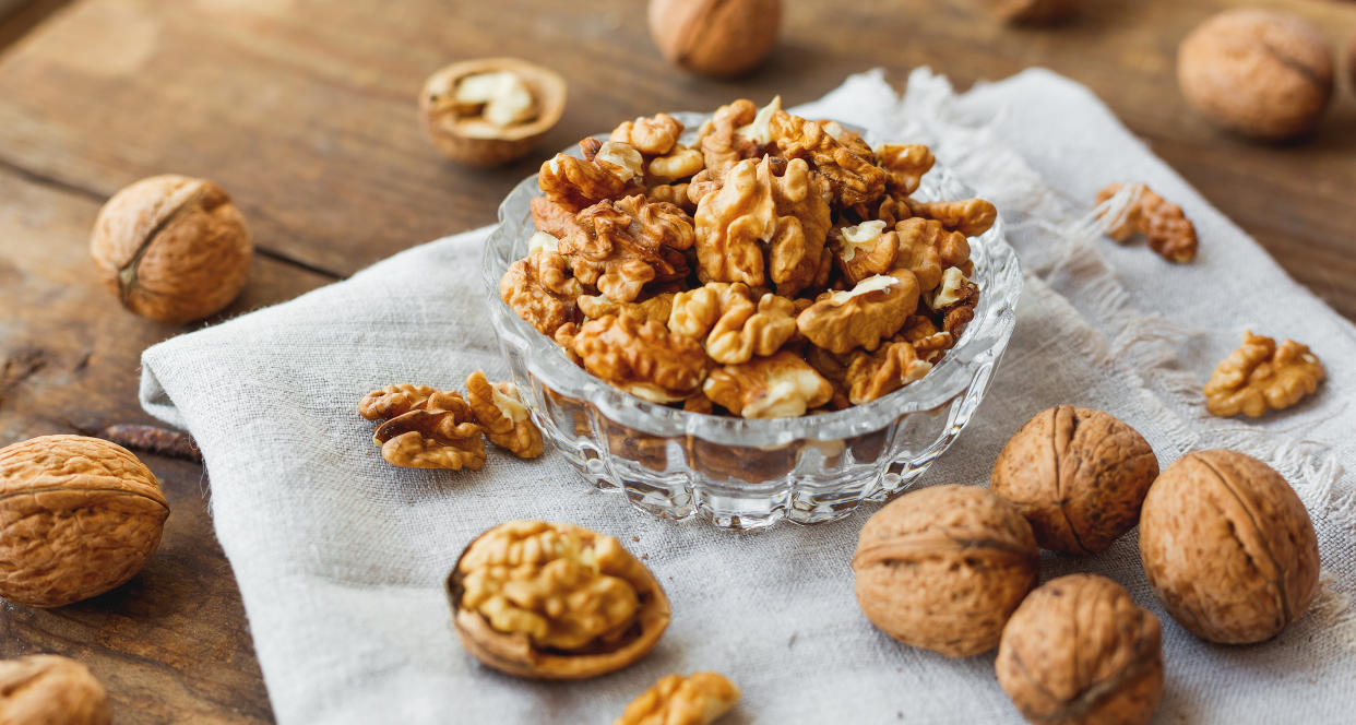 Glass bowl with walnuts on rustic homespun napkin. Healthy snack on old wooden background.