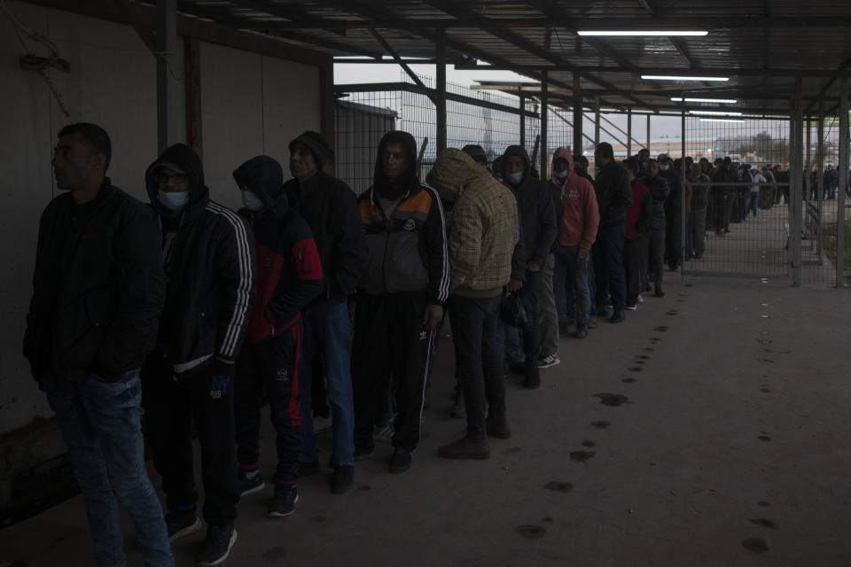 Palestinian workers line up while waiting at the Palestinian side of Erez crossing to cross to Israel, in the town of Beit Hanoun, northern Gaza Strip, March. 27, 2022. Israel said it will reopen its crossing with the Gaza Strip to Palestinian workers on Tuesday, April 26, 2022, after it had been closed for several days following rocket attacks from the Palestinian enclave. Israel has issued thousands of work permits to Palestinians from Gaza, which has been under a crippling Israeli and Egyptian blockade since Hamas seized power from rival Palestinian forces nearly 15 years ago. (AP Photo/Khalil Hamra)