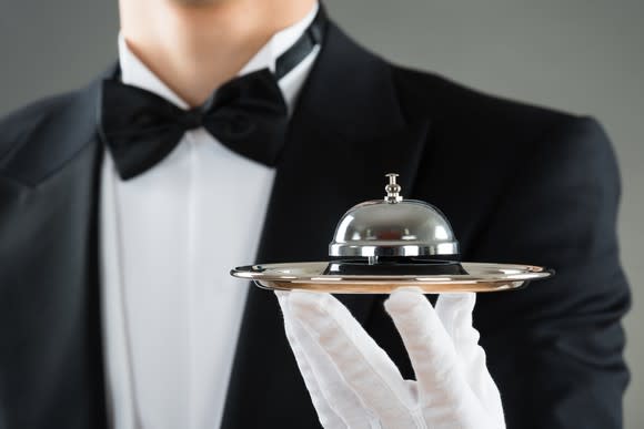 White-gloved waiter holding service bell on plate