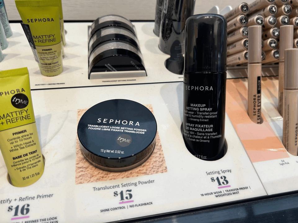 Self of Sephora beauty items in store. From left to right, a yellow tube of Sephora mattify and refine primer, a black container of translucent setting powder, and a black container of setting spray are on display